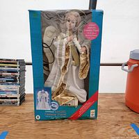 Full front view of boxed animated angel figurine approx. 2 feet tall with white and gold garments visible through clear plastic window.