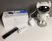 Astronaut starry sky projector with USB cable and remote control laid out next to the box on a white surface.