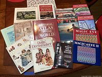 Overhead view of 14 assorted books including topics of doll dressmaking, photography, wine, gardening, and world atlas.
