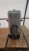 Photo of the coffee maker standing upright with power cord wrapped around spout and handles visible