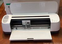 Open front view of Cricut Maker showing dual blade holders inside the machine with hinged cover open.