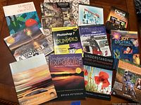 Top view of twelve photography books arranged on a wooden surface showing titles and cover art.