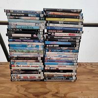 Photo showing 49 DVD cases stacked in two piles on a wooden floor with various movie titles visible on the spines.