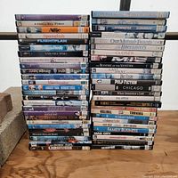 Photo of two tall stacks of assorted DVD movie cases on wooden floor showing many different movie titles.