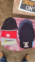 Set of six beanies and headwear pieces displayed on surface, showing variety of colors and logos.