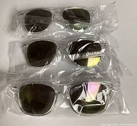 Three pairs of UV rated sunglasses individually sealed in clear plastic packaging shown on a white background.