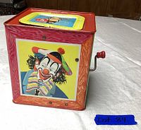 Photo of the metal box with colorful clown artwork and side crank handle on table.
