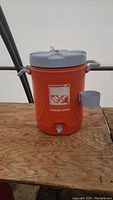 Orange 20 liter cooler with blue lid and cup, Home Depot logo, and spigot for drinking water.