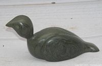 Side view of dark green soapstone loon sculpture showing smooth finish, engraved wing and eye details, and natural stone patterns.