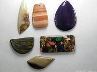 Top view showing the six polished natural stone pendants in various shapes and colors, all with drilled holes for wearing.