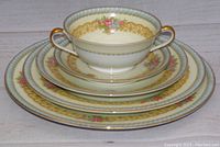 Stacked breakfast set including two handled cup, saucers, bread and butter plate, salad plate, dinner plate, all with floral and gold detailing.