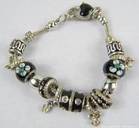Full bracelet laid flat showing black cloisonne flower beads, rhinestone bead and silver-tone spacers with dangling charms.