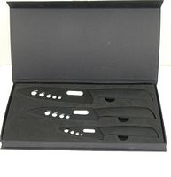 Three black ceramic knives with white apple designs on the blades arranged in a black foam insert box.