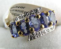 Close-up photo of sterling silver ring with five oval faceted tanzanite stones and white topaz accents in gold plated prong settings.