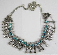 Front view of a silver-tone tribal style necklace with triangular metal pendants and blue stones.