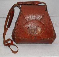 Front view of vintage tooled leather handbag showing flap and strap closure, leather shoulder strap with padded section.
