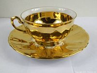 Side angle of the vintage gold-tone cup resting on the matching saucer showing the lustrous finish and textured saucer edges.