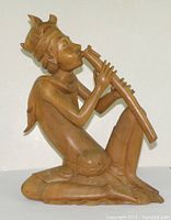 Side view of a seated wooden sculpture playing a flute, showing detailed carving of the headdress and legs
