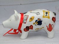 Side view of the white ceramic piggy bank in the shape of a pig showing colorful illustrations and red ribbon tied around the neck.