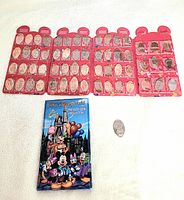 Two Walt Disney World pressed coin folders laid flat. Red folder fully loaded with pressed coins. Blue folder closed with visible cover art and some coins nearby.