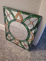 Photo of stained glass framed mirror leaning against wall on carpeted floor.