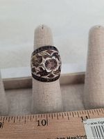 Front view of large costume jewelry ring on display stand with ruler for size reference showing floral and leaf pattern.