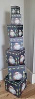 Stack of 7 Christmas storage boxes with lids, each decorated with Santa Claus images and holly borders, stacked from largest to smallest.