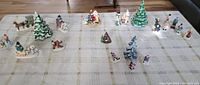 Full view of assorted Christmas-themed miniatures arranged on a table, including decorated trees, Santa figurines, winter clad human figures, campfire, and animals.