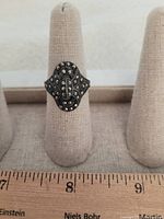 Close-up view of the costume jewelry ring placed on a beige ring display stand with a ruler showing about a size 8-9 approximate measurement.