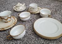 Overall view of vintage Rosenthal Bavaria Madeleine hand-painted tea set with gold trim, including teapot, cups, saucers, plates, and extra mismatched china pieces all placed on carpeted floor.