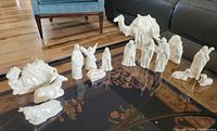 Photo of a white ceramic nativity set laid out on a table including human and animal figures.