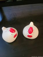 Pair of white ceramic rooster head salt and pepper shakers with red comb and beak details shown on dark surface.