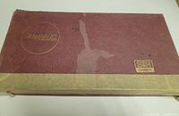 Rectangular maroon and gold Scrabble box with visible wear and damage.