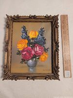 Oil painting of floral still life with yellow, pink, and purple flowers in white vase, signed G. Moses with ornate carved wood frame, ruler for scale
