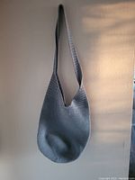 Grey hand-crochet purse hanging on wall, showing full strap and rounded bottom shape.