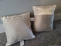 Two small decorative throw pillows placed upright on carpet floor against wall to show front designs