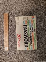 Top view of the vintage MB Password 20th Edition board game box from 1978 on carpet background. Shows colorful text collage with edition and MB logo.