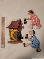 Photo of three vintage hand-painted ceramic bathroom wall decor pieces showing distinct characters and a house with a moon, placed beside a 12-inch ruler for scale.