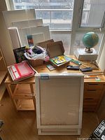 Wide view of lot showing multiple stretched canvases leaning, art and craft supplies on table including yarn, colored pencils, globe, and various tools.