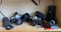 Wide shot of two Pentax Spotmatic cameras, Vivitar zoom lens, cases, filters, wrench and manual on shelf