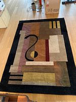 Full view of the rectangular rug on a wooden floor showing its geometric abstract pattern and colors.