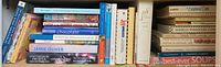 Spine view of multiple assorted cookbooks stacked horizontally and vertically showing variety of titles related to cooking, soups, uncommon vegetables, chocolate, Jamie Oliver, and more.
