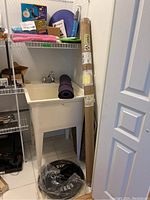 Wide shot showing the weight plates, yoga mat, twist board, fit ball, and the packaged Olympic weight bar leaning against a sink in a storage or laundry room.