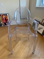 Front view of clear plastic ghost chair with armrests, showing rounded backrest and seat.