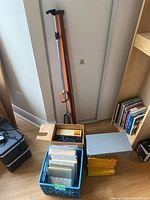 Full lot view showing slide carousel unit with slide trays inside original box, metal slide boxes, projector screen on tripod, and milk crate filled with photo sleeves.