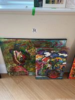 Both abstract acrylic paintings positioned leaning against a wall on the floor, showing size comparison and color palette.