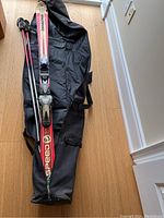 Photo showing the skis with bindings laid on the black carry bag, with two pairs of ski poles visible.
