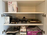 Shelf showing Master Chef electric kettle box, toaster, Salton induction cooktop box, Osterizer blender base, Breville panini press, cutter sharpener, and electric griddle.