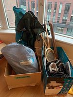 Aerobed inflatable mattress in storage bag, folding camping chairs, rollerblades, badminton rackets, and walking sticks visible in boxes by window