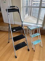 Side view of both folding step stools, black and turquoise, showing size difference and general condition